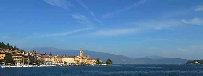 Trip Rooms beliebte Urlaubsziele am Gardasee -  Mit einer Fläche von 370 km² ist der Gardasee der größte See Italiens. Es liegt am Fuße der Alpen und erstreckt sich über drei Staaten: Lombardei, Venetien und Trentino. Die maximale Tiefe des Sees beträgt 346 m, er hat eine längliche Form und sein nördliches Ende ist sehr schmal. Dort ist der See von den Bergen der Gruppo di Baldo umgeben. Du trittst aus deinem gemütlichen Hotelzimmer und es begrüßt dich die warme italienische Sonne. Du blickst auf den atemberaubenden Gardasee, der in zahlreichen Blautönen schimmert - von tiefem Dunkelblau bis zu funkelndem Türkis. Majestätische Berge umgeben dich, während die Brise sanft deine Haut streichelt und der Duft von blühenden Zitronenbäumen deine Nase kitzelt. Du schlenderst die malerischen, engen Gassen entlang, vorbei an farbenfrohen, blumengeschmückten Häusern. Vereinzelt unterbricht das fröhliche Lachen der Einheimischen die friedvolle Stille. Du fühlst dich wie in einem Traum, der nicht enden will. Jeder Schritt führt dich zu neuen Entdeckungen und Abenteuern. Du probierst die köstliche italienische Küche mit ihren frischen Zutaten und verführerischen Aromen. Die Sonne geht langsam unter und taucht den Himmel in ein leuchtendes Orange-rot - ein spektakulärer Anblick.